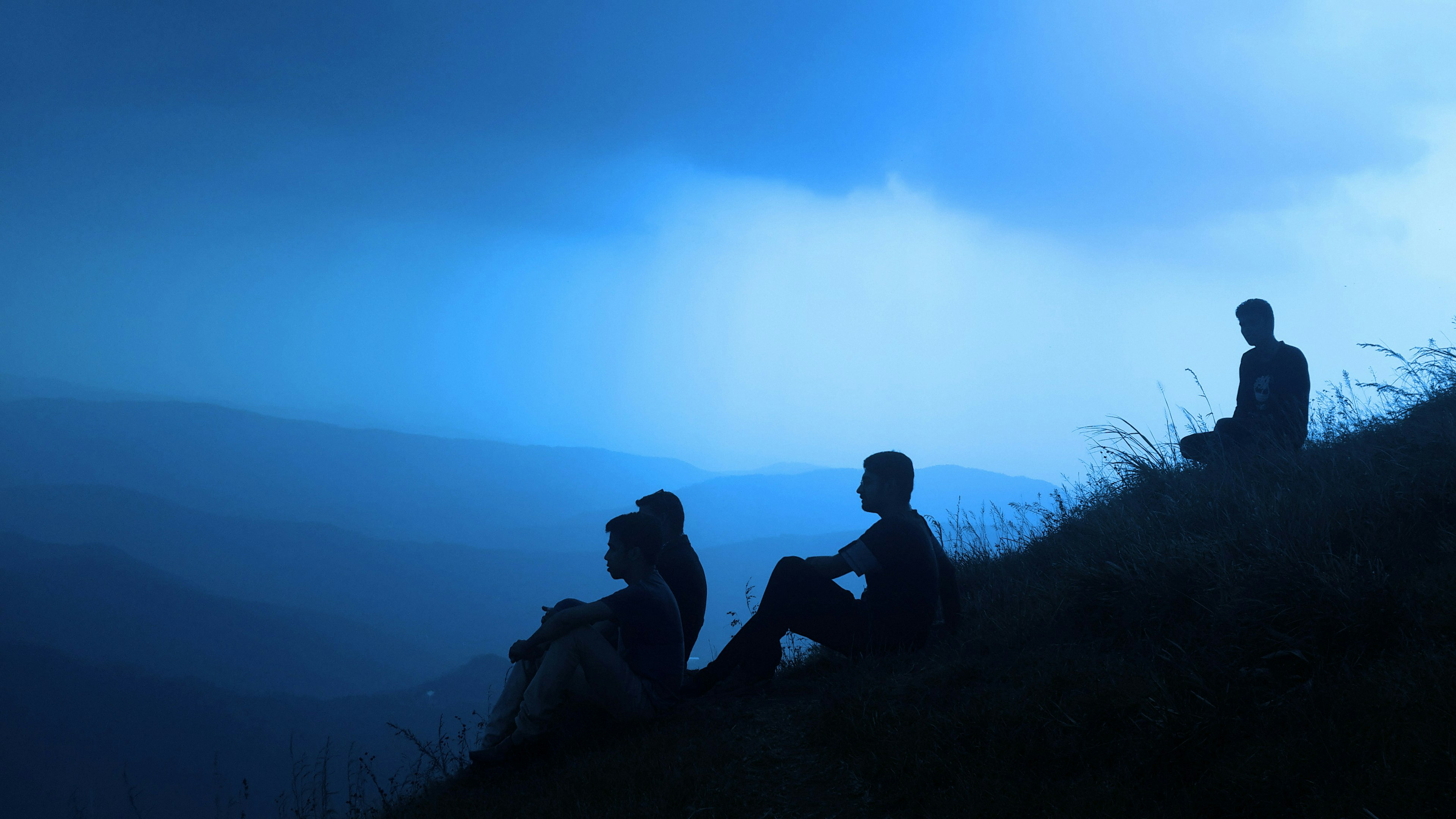 Silhouettes of people sitting on a hill. Its dark.